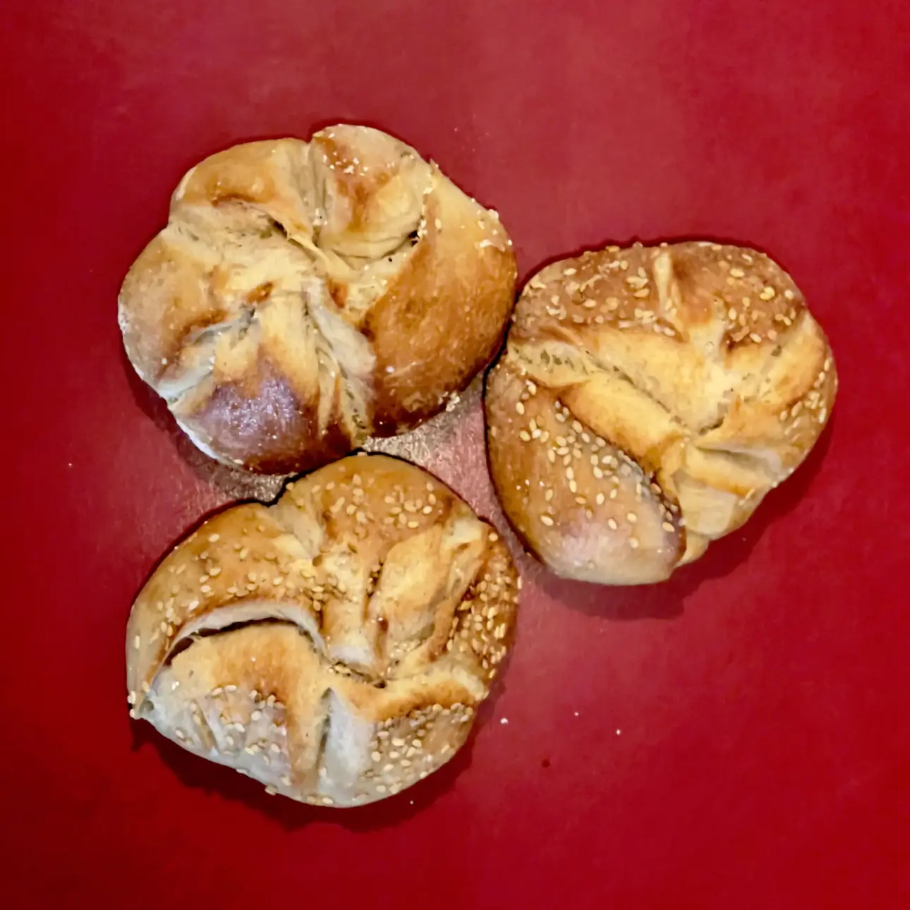Drei kleine Brötchen mit Sesam auf einem roten Teller.