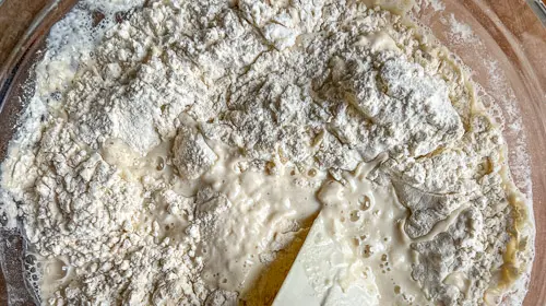Ein gläserner Behälter enthält einen Sauerteigbrotteig mit Mehl und Flüssigkeit.