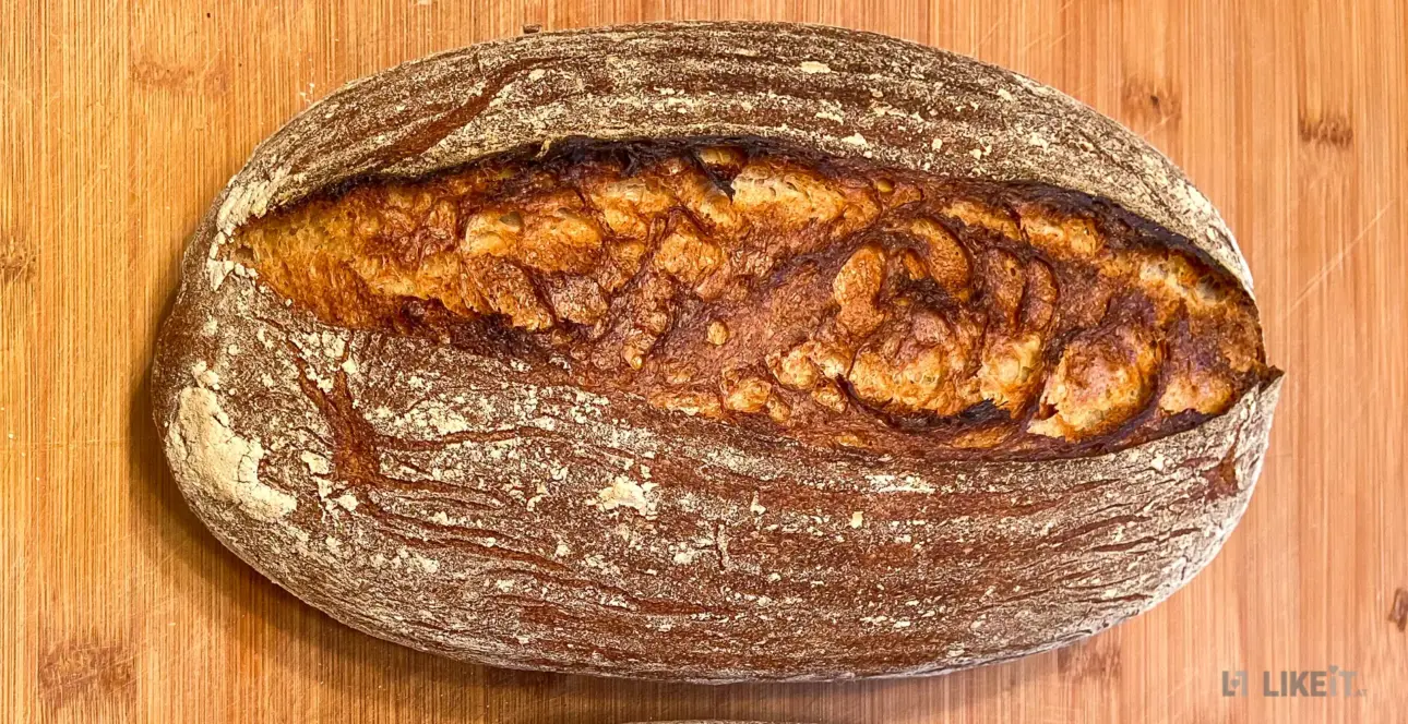 Ein frisch gebackenes Sauerteig-Brot liegt auf einem Holzbrett. Es hat eine goldbraune Kruste.
