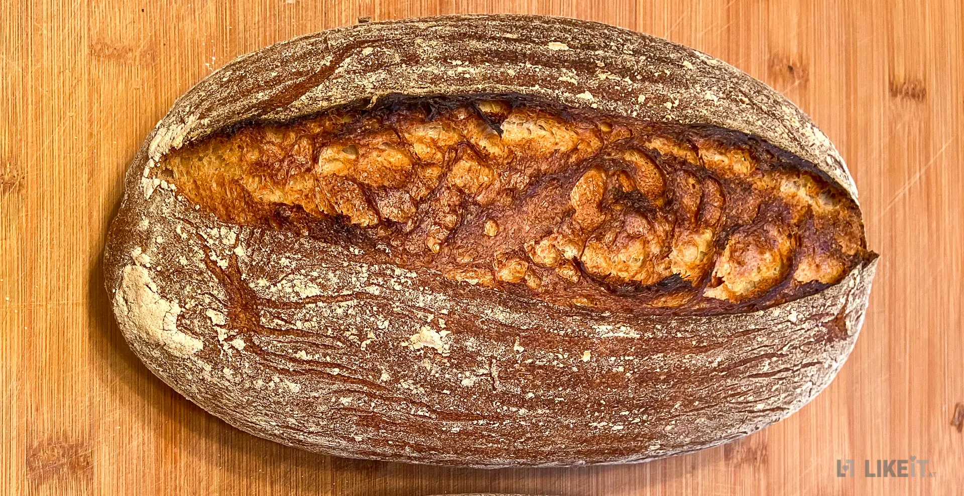 Ein frisch gebackenes Sauerteig-Brot liegt auf einem Holzbrett. Es hat eine goldbraune Kruste.