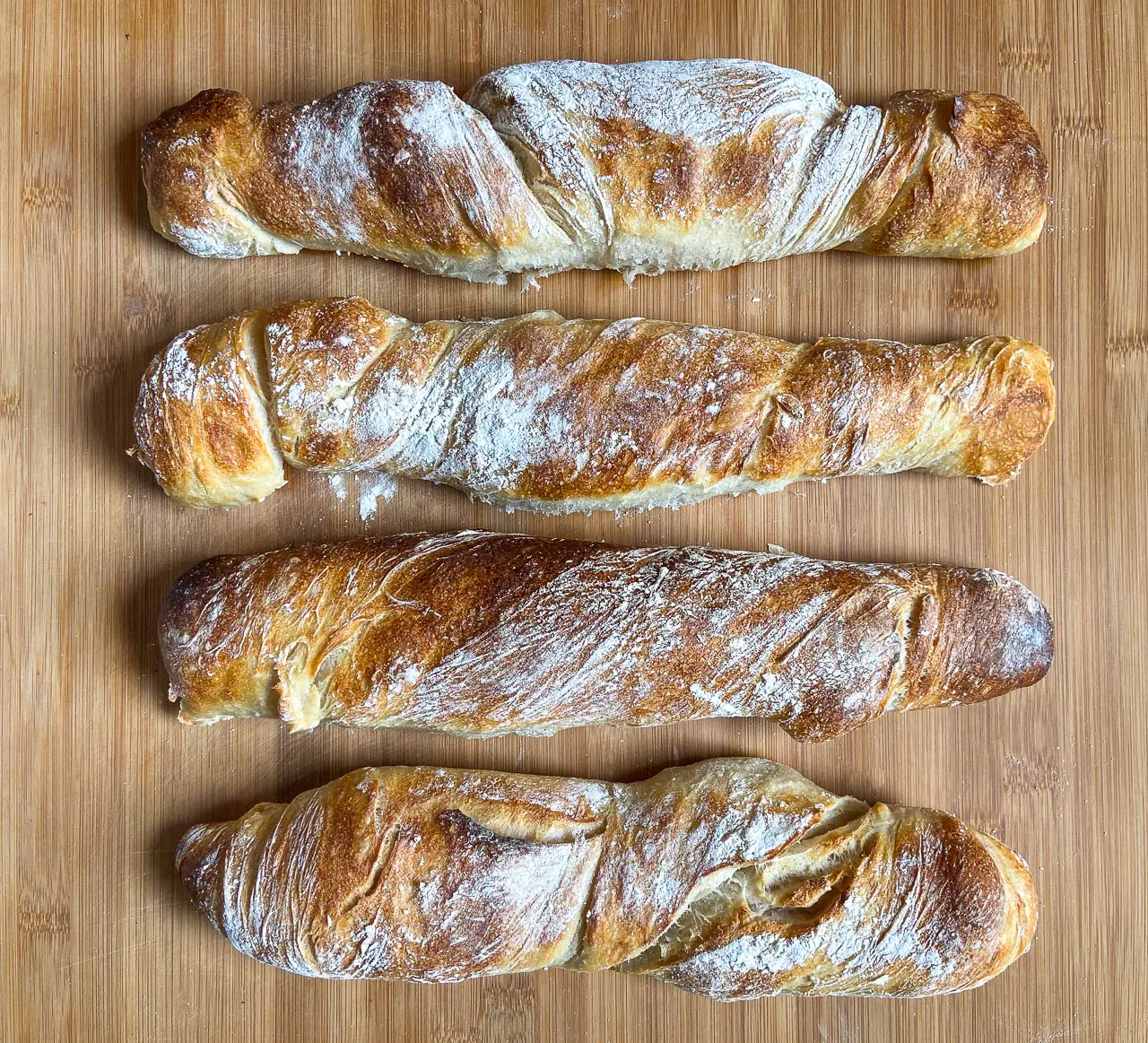 Vier langgestreckte Brote mit Kreuzschnitt auf einem Holzbrett